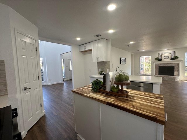 kitchen featuring butcher block counters, white cabinetry, dark hardwood / wood-style flooring, stainless steel dishwasher, and decorative backsplash