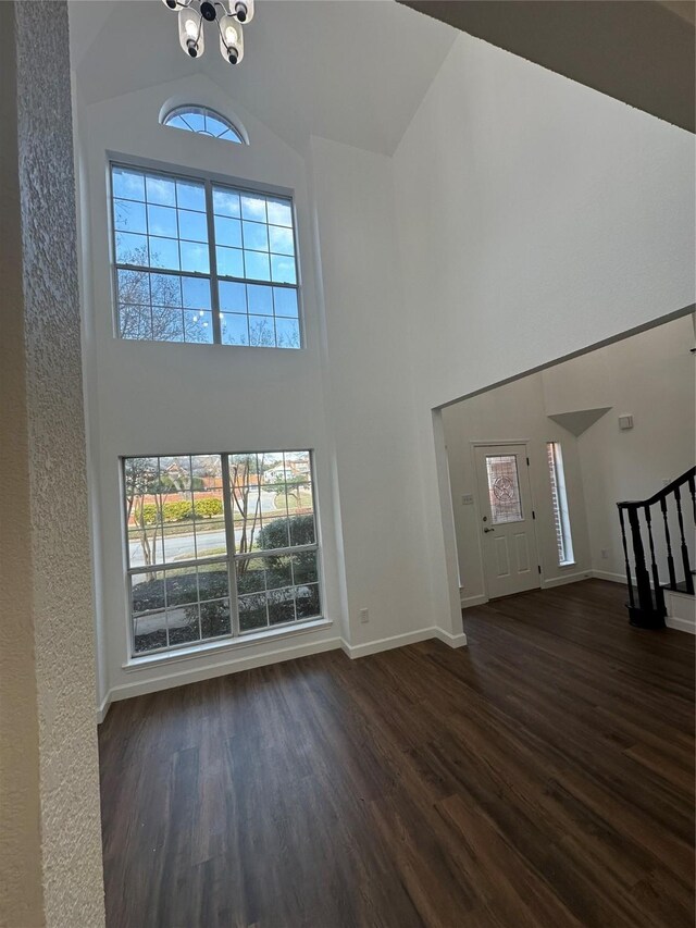 unfurnished living room with high vaulted ceiling and dark wood-type flooring