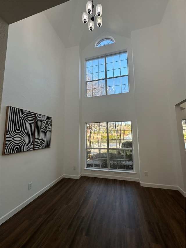 unfurnished living room with dark hardwood / wood-style flooring, high vaulted ceiling, and an inviting chandelier