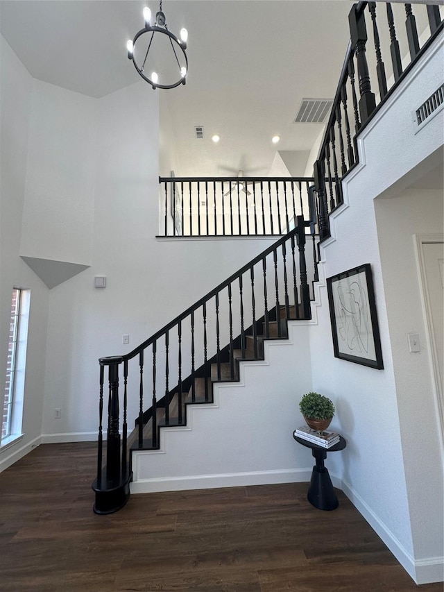 stairs with hardwood / wood-style floors, a notable chandelier, and a towering ceiling