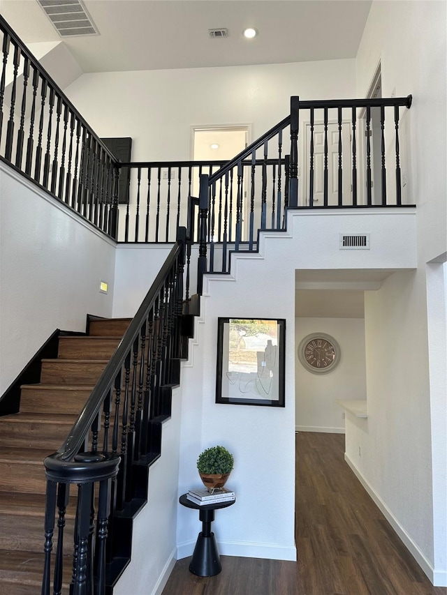 stairs with wood-type flooring and a towering ceiling