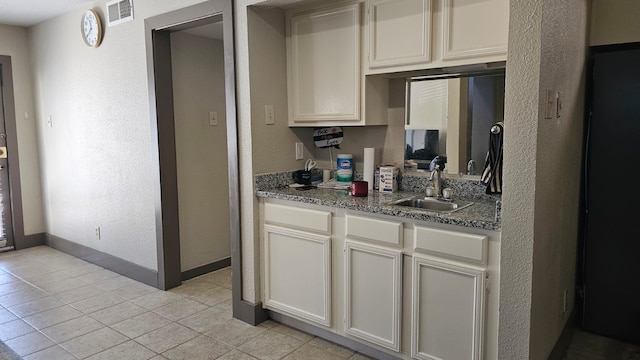 kitchen featuring white cabinets, sink, light tile patterned floors, and stone countertops