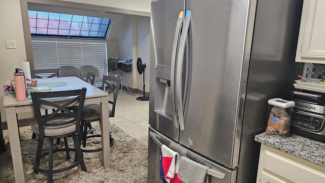 kitchen featuring lofted ceiling, stainless steel refrigerator with ice dispenser, light stone countertops, light tile patterned floors, and white cabinetry