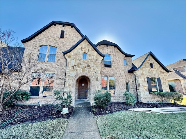 french country home featuring stone siding and brick siding