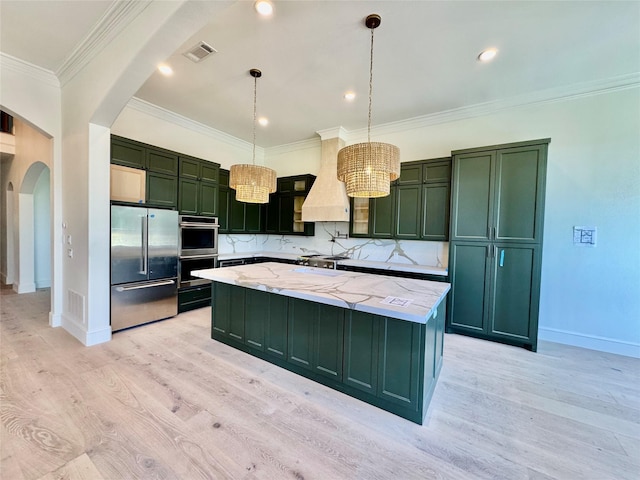 kitchen featuring arched walkways, green cabinets, custom range hood, and appliances with stainless steel finishes