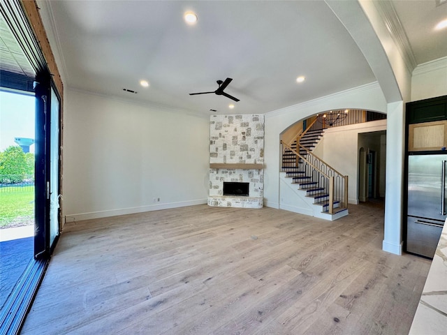 unfurnished living room featuring a wealth of natural light, light wood-type flooring, ceiling fan, stairway, and crown molding