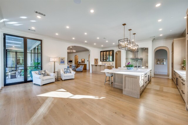 kitchen featuring light brown cabinetry, crown molding, a large island with sink, decorative light fixtures, and light hardwood / wood-style floors