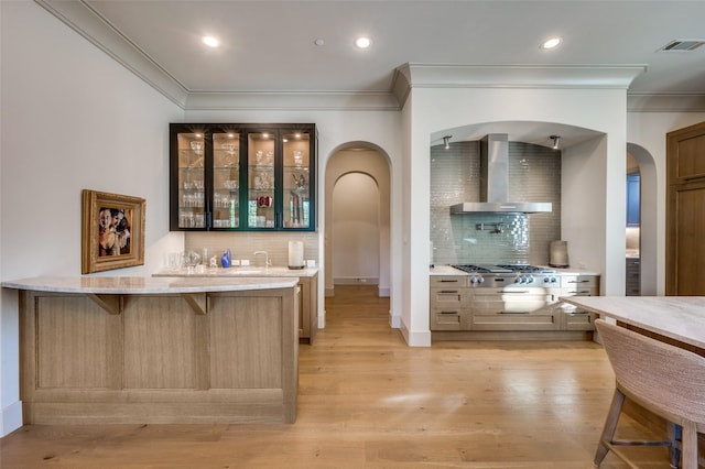 kitchen featuring a kitchen breakfast bar, tasteful backsplash, ornamental molding, wall chimney exhaust hood, and light hardwood / wood-style flooring