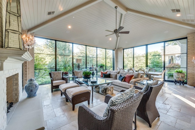 sunroom featuring vaulted ceiling with beams, plenty of natural light, an outdoor brick fireplace, and ceiling fan with notable chandelier