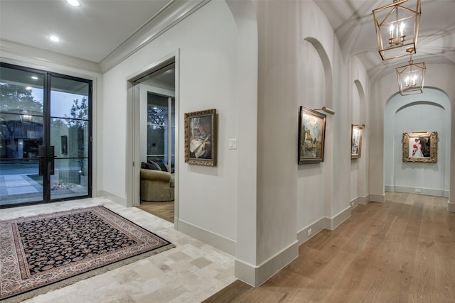 hallway with crown molding, light wood-type flooring, and a notable chandelier