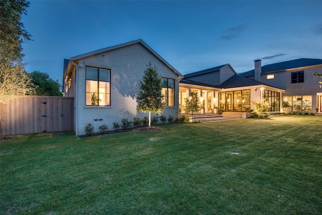 back house at dusk featuring a lawn