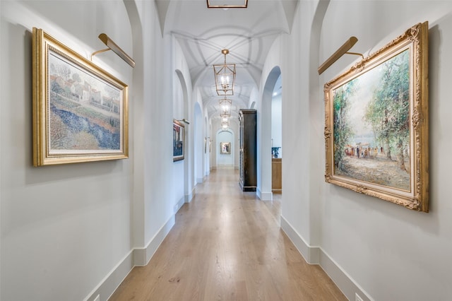 corridor with light hardwood / wood-style flooring, vaulted ceiling, and a notable chandelier