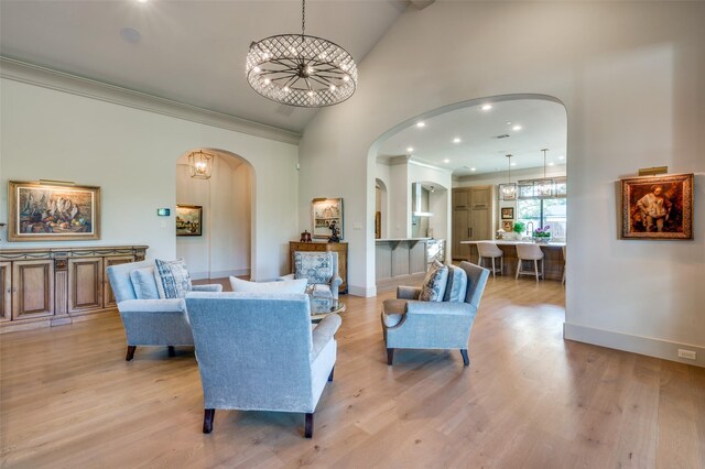 living room featuring a notable chandelier, crown molding, high vaulted ceiling, and light hardwood / wood-style flooring