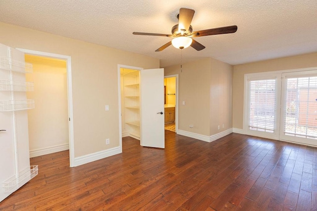 unfurnished bedroom with a textured ceiling, a walk in closet, dark hardwood / wood-style flooring, a closet, and ceiling fan