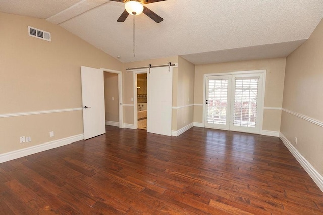 spare room featuring a textured ceiling, lofted ceiling, dark hardwood / wood-style floors, ceiling fan, and a barn door