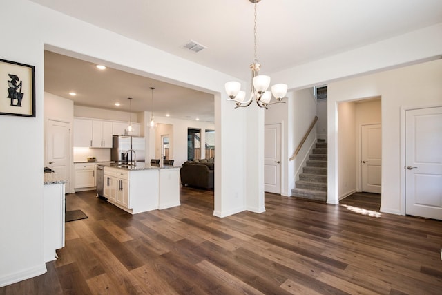 kitchen featuring appliances with stainless steel finishes, dark hardwood / wood-style floors, pendant lighting, white cabinets, and a center island with sink