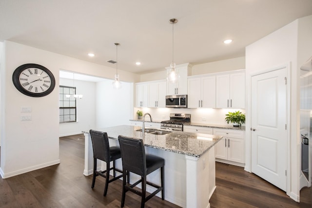 kitchen with sink, white cabinetry, appliances with stainless steel finishes, light stone countertops, and a kitchen island with sink