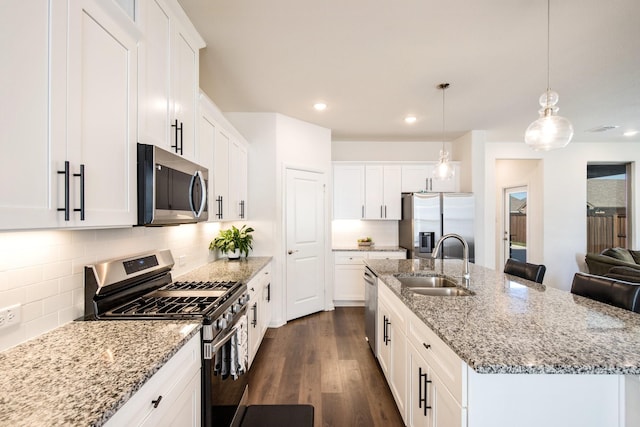 kitchen with appliances with stainless steel finishes, pendant lighting, white cabinetry, sink, and a center island with sink