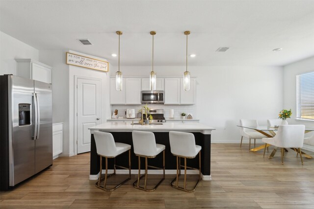 kitchen featuring white cabinets, decorative light fixtures, light hardwood / wood-style floors, and stainless steel appliances