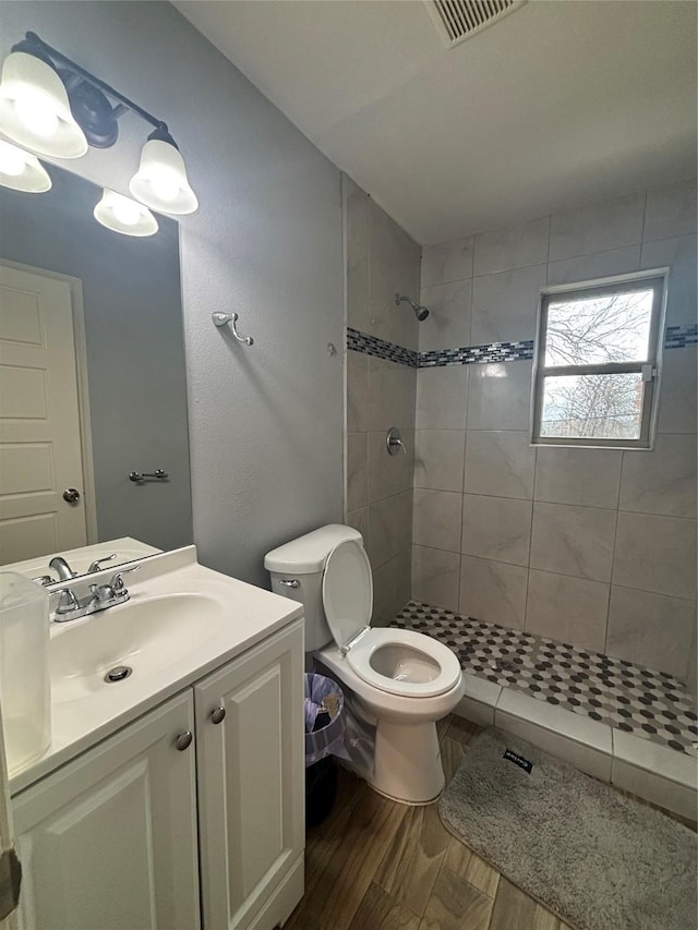 bathroom with tiled shower, hardwood / wood-style floors, vanity, and toilet