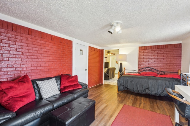 bedroom with wood-type flooring, a textured ceiling, and brick wall