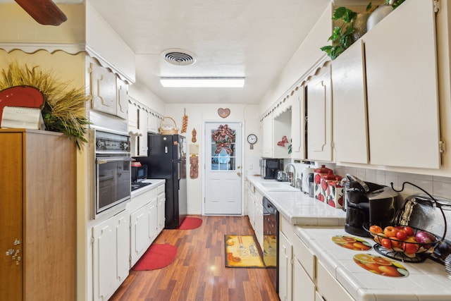 kitchen featuring sink, dark hardwood / wood-style floors, tile countertops, white cabinets, and black appliances