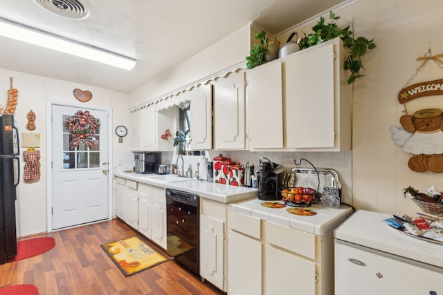 kitchen with black appliances, white cabinets, sink, decorative backsplash, and light wood-type flooring