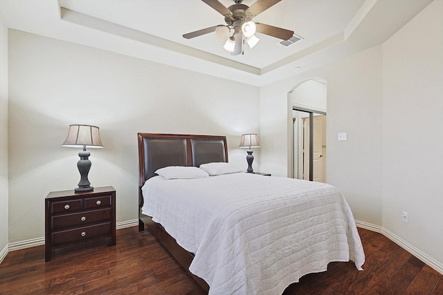 bedroom featuring a raised ceiling, dark wood-type flooring, ceiling fan, and a closet