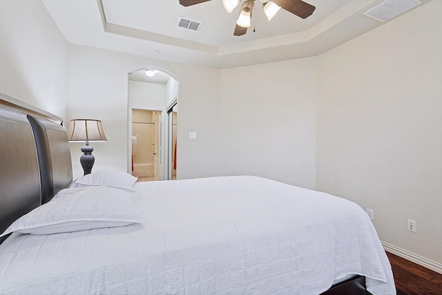 bedroom featuring dark hardwood / wood-style floors, ceiling fan, connected bathroom, and a tray ceiling