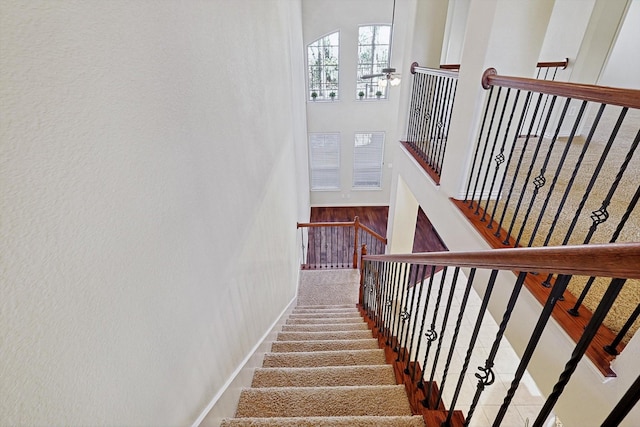 staircase with a ceiling fan, a high ceiling, and baseboards