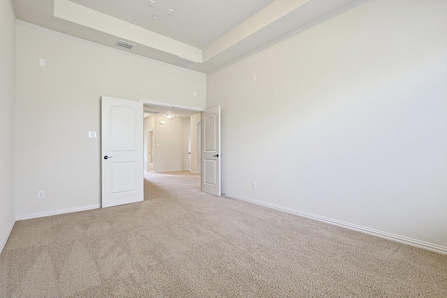 carpeted empty room with a raised ceiling, visible vents, and baseboards