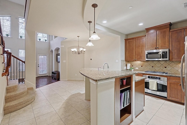 kitchen with tasteful backsplash, light stone counters, a kitchen island with sink, stainless steel appliances, and open shelves