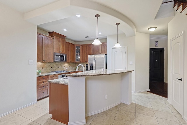 kitchen with decorative light fixtures, an island with sink, stainless steel appliances, light stone countertops, and decorative backsplash