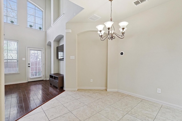 tiled entrance foyer with visible vents, a notable chandelier, and baseboards