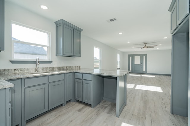 kitchen featuring light stone counters, sink, gray cabinets, and kitchen peninsula