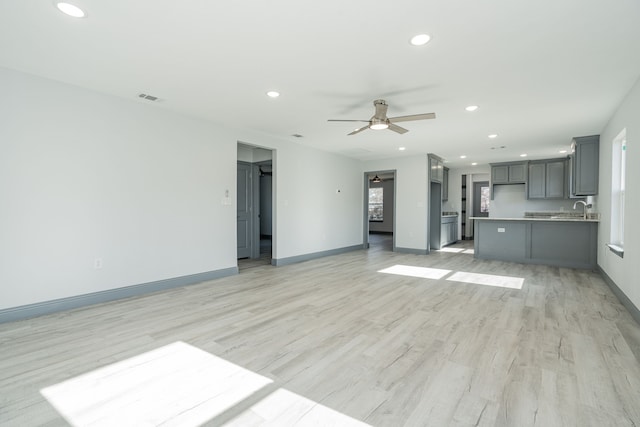 unfurnished living room featuring light hardwood / wood-style floors, ceiling fan, and sink