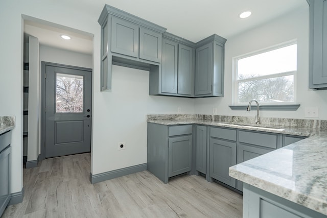 kitchen with gray cabinets, light stone countertops, sink, and light hardwood / wood-style flooring