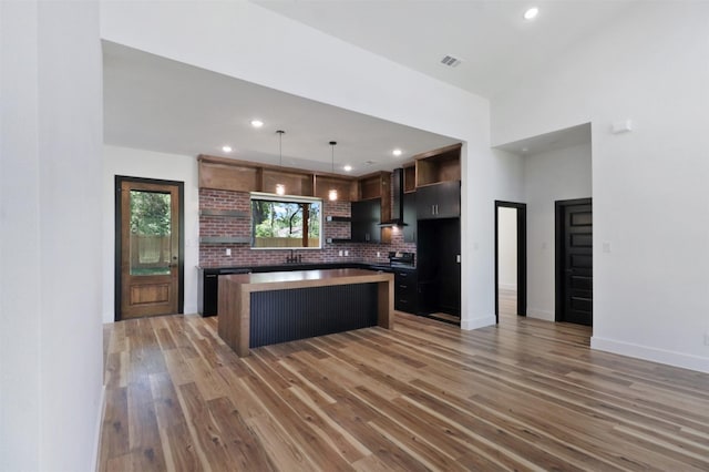 kitchen featuring a center island, wall chimney exhaust hood, tasteful backsplash, dark hardwood / wood-style floors, and pendant lighting