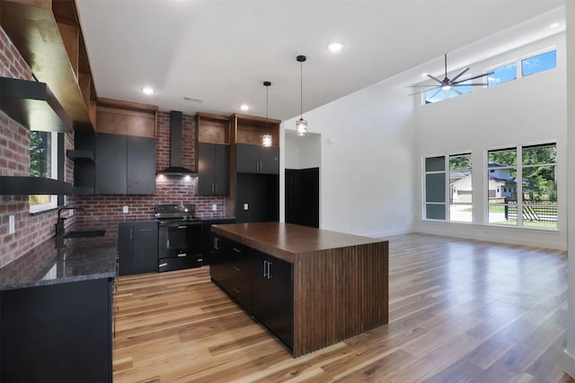 kitchen featuring sink, wall chimney range hood, light hardwood / wood-style floors, a kitchen island, and black / electric stove