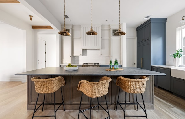 kitchen featuring backsplash, hanging light fixtures, light hardwood / wood-style flooring, a large island, and a breakfast bar area