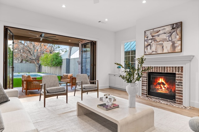 living room featuring a brick fireplace, light hardwood / wood-style flooring, and ceiling fan