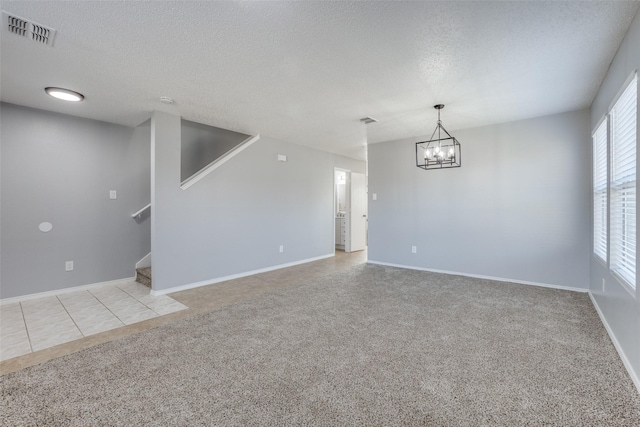 carpeted spare room with a chandelier and a textured ceiling