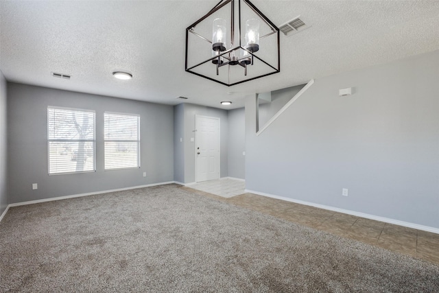 spare room featuring carpet floors, a chandelier, and a textured ceiling