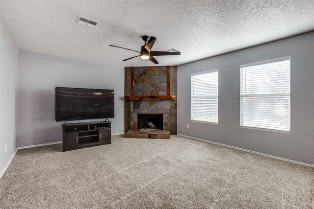 carpeted living room with a textured ceiling, a stone fireplace, and ceiling fan