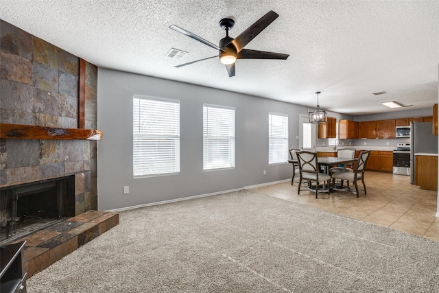 interior space featuring a textured ceiling, a tiled fireplace, a wealth of natural light, and ceiling fan with notable chandelier