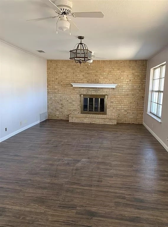 unfurnished living room featuring ceiling fan with notable chandelier, dark hardwood / wood-style floors, a brick fireplace, and brick wall