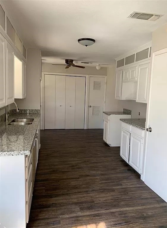 kitchen featuring white cabinetry, sink, ceiling fan, light stone countertops, and dark wood-type flooring