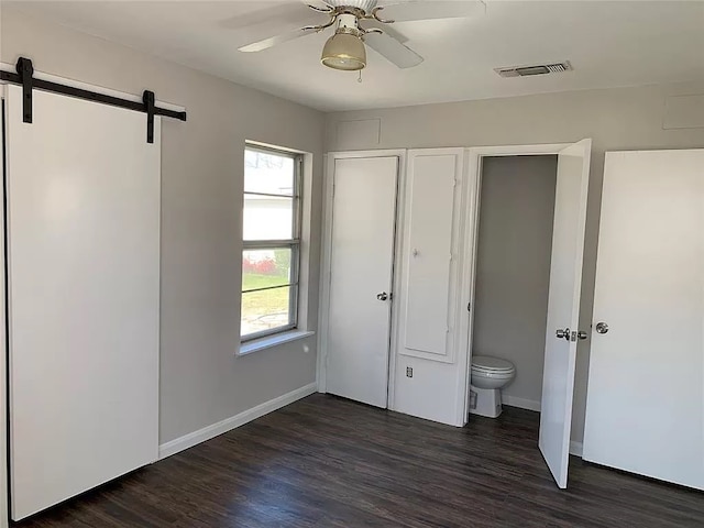 unfurnished bedroom featuring ceiling fan, a barn door, and dark hardwood / wood-style flooring