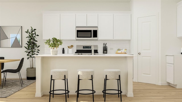 kitchen featuring backsplash, white cabinets, a kitchen breakfast bar, stainless steel range, and light hardwood / wood-style floors