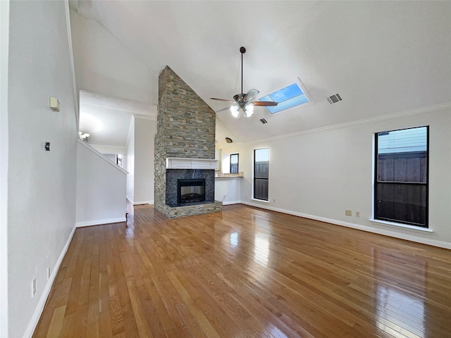 unfurnished living room with hardwood / wood-style flooring, high vaulted ceiling, a skylight, and a stone fireplace